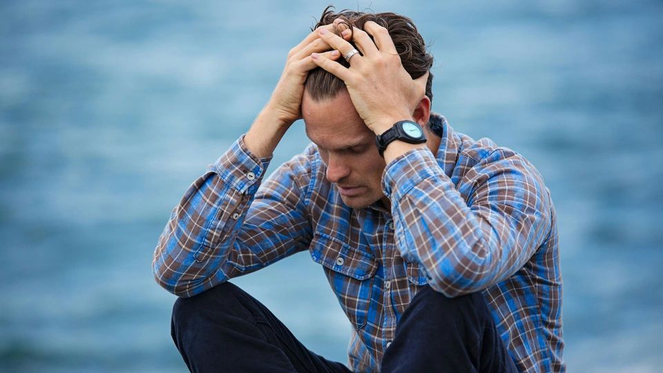 A man in a plaid shirt runs his hands through his hair, looking anxious.