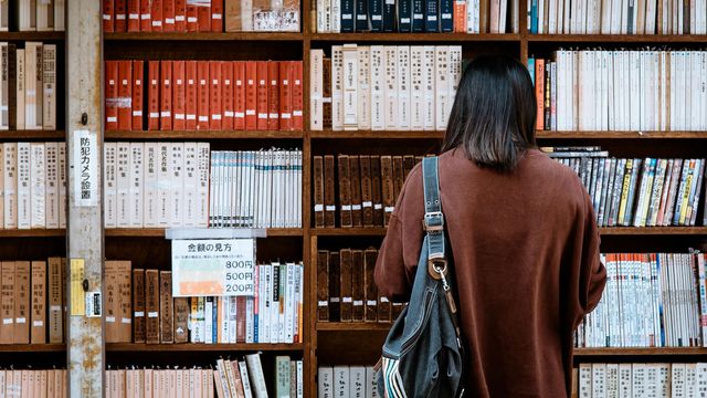 A person with long dark hair in a library, choosing books. 