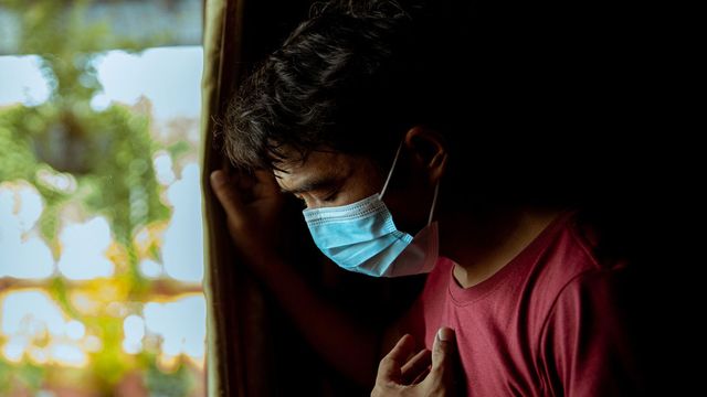 Individual wearing a blue surgical mask coughing. 