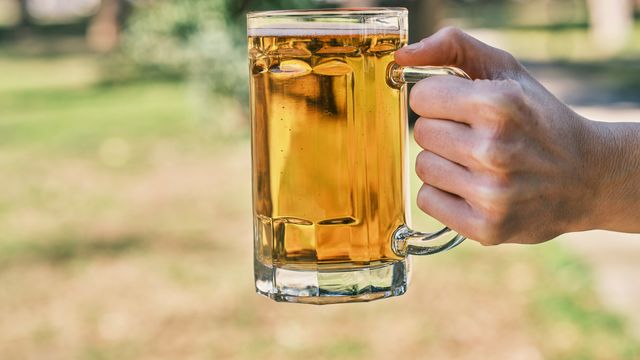 A man holding a large stein of beer, outside. 