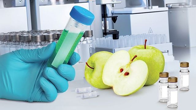 Gloved hand holding vial near green apples and lab instruments, illustrating micro-SPE technology for optimizing food safety testing. 