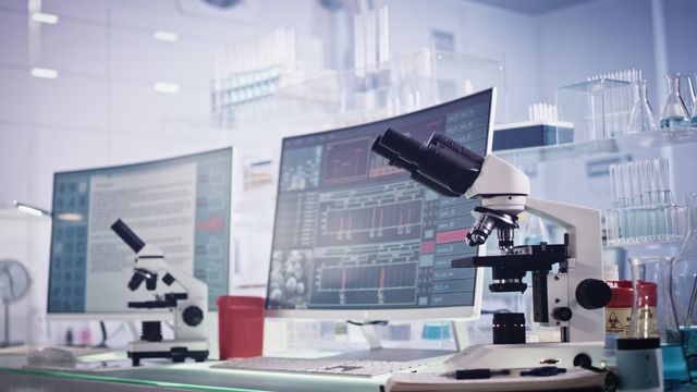 Custom LIMS dashboard shown on lab monitors beside microscopes in a modern research lab. 