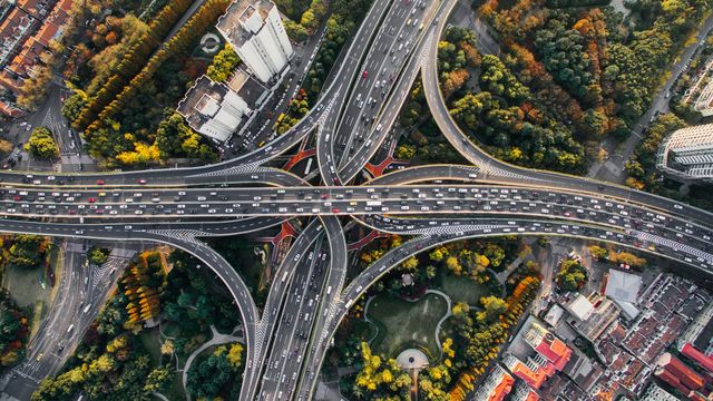 An aerial photo of a complex highway interchange in a city, surrounded by tall buildings and green trees. 